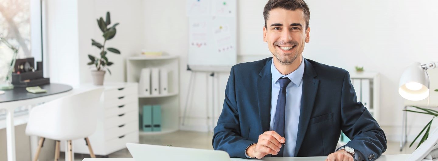 Junger Banking Manager sitzt lächelnd am Schreibtisch