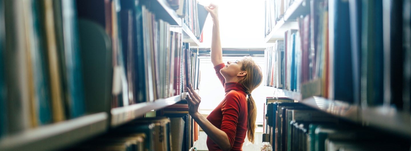 Junge Bibliothekarin nimmt Buch aus einem Regal