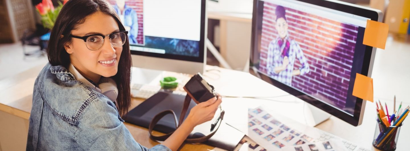 Foto Designer Weiterbildung: eine junge Foto Designerin sitzt am PC und lächelt in die Kamera