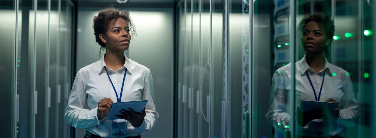 IT-Servicetechniker Weiterbildung: eine IT-Servictechnikerin steht mit einem Tablet in einem Serverraum