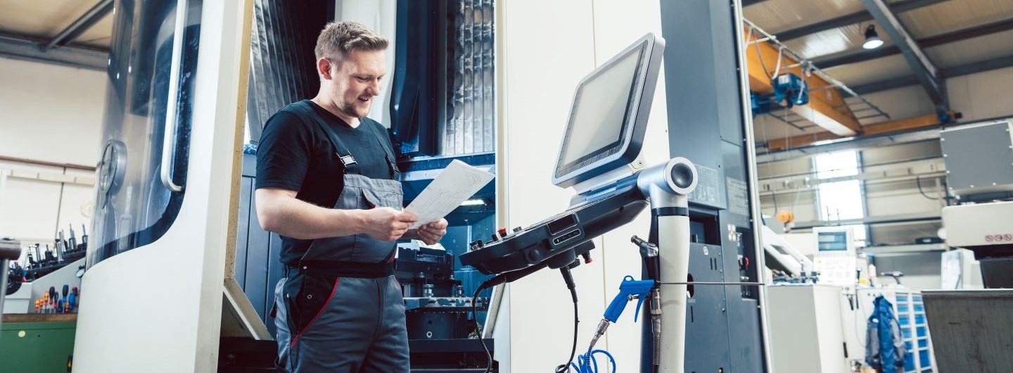 NC- und CNC-Technik Weiterbildung: Ein Arbeiter in der Metallindustrie bedient eine moderne CNC-Anlage