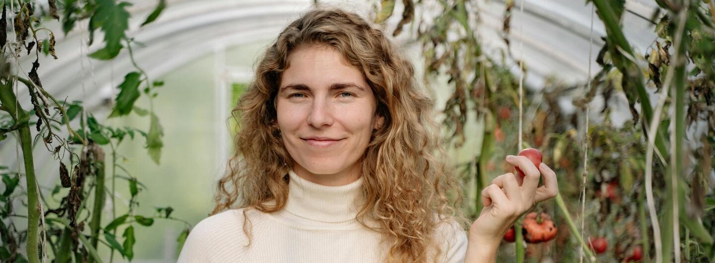 Eine junge Gärtnerin steht im Gewächshaus und hält Paprika in die Kamera.