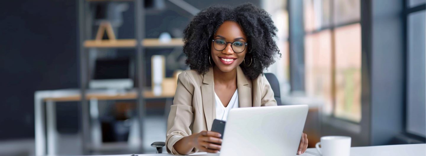 User Experience Manager Weiterbildung: eine User Experience Managerin sitzt an ihrem Laptop und hält ein Smartphone in der Hand