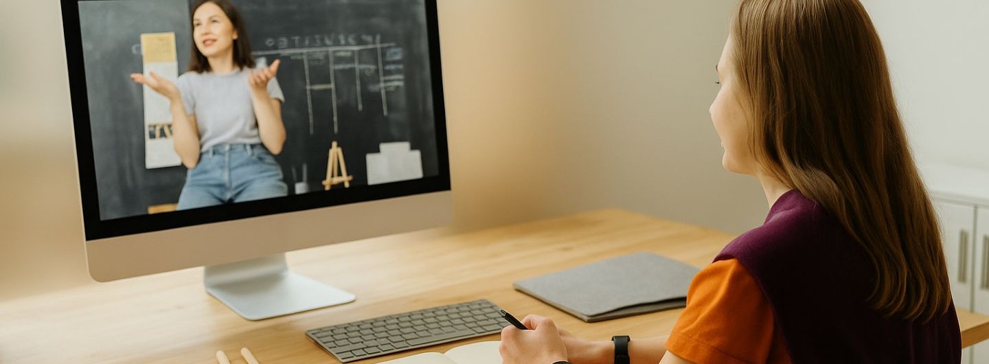 eine junge Frau sitzt vor einem Monitor und verfolgt einen Online-Sprachkurs