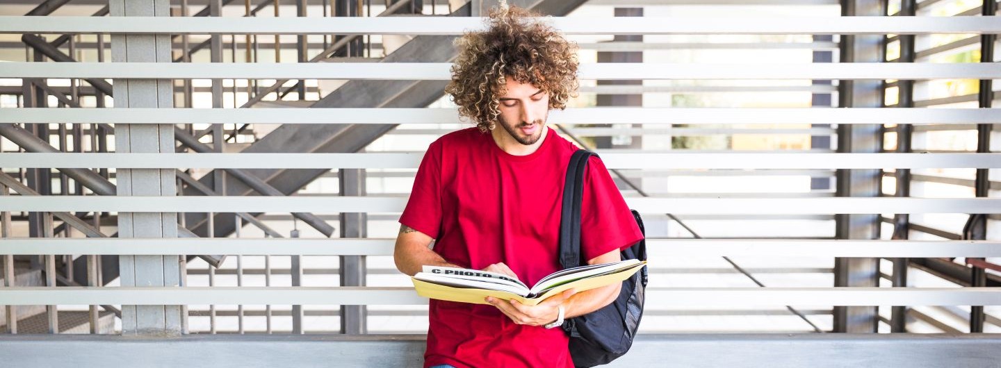 ein Student lehnt an einer Wand und liest in einem Buch